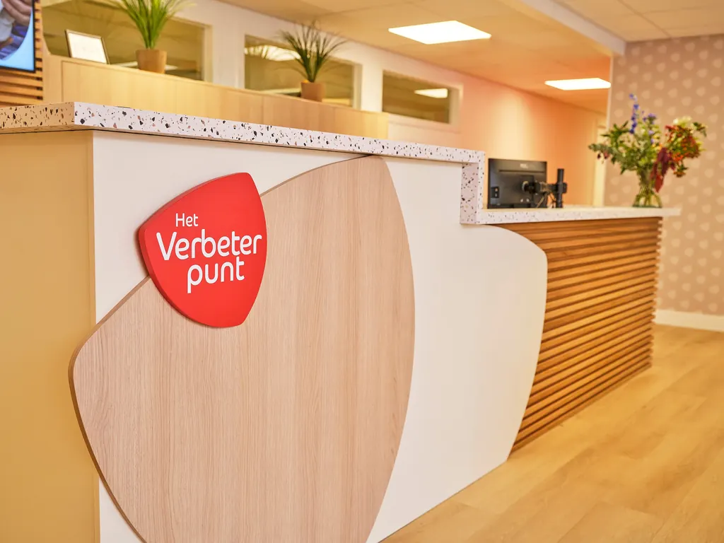 De ontvangstbalie van Het Verbeterpunt, met het rode logo op een houten punt-vorm