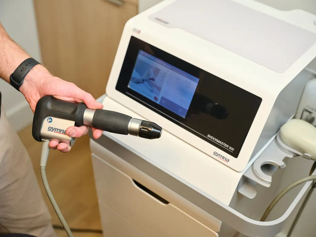 Een fysiotherapeut houdt de handgreep van het shockwave-apparaat vast