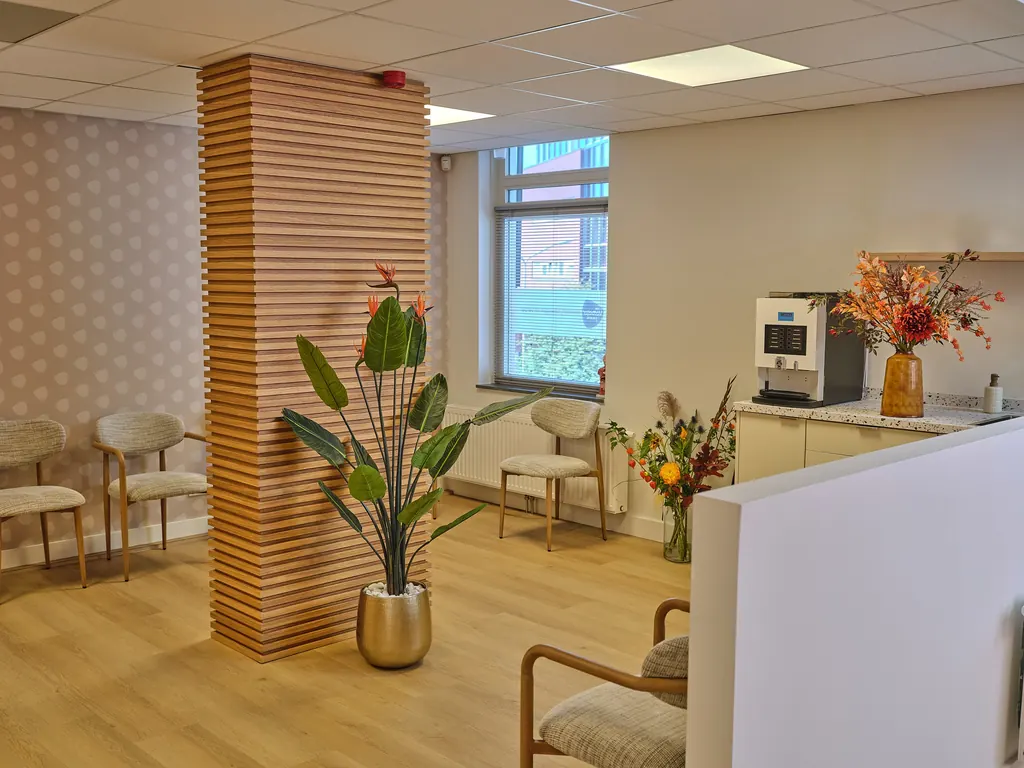 De lichte wachtruimte met stoelen, planten en een koffieautomaat